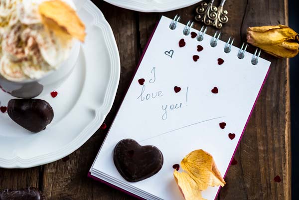 cappuccino with a note saying i love you and heart shaped chocolate with confetti shaped hearts