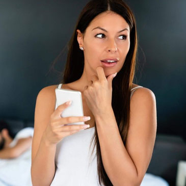 woman talking privately on her cellphone and looking guilty of something while her husband-sleeps